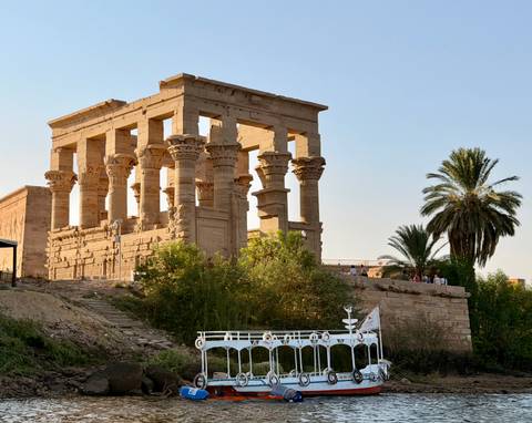       Ancient sandstone kiosk-style temple ruins beside the Nile with lush shrubs and evening sunlight
  