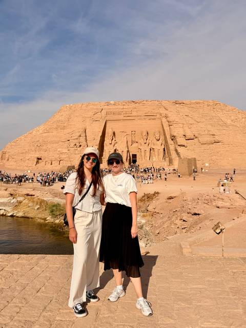       Two smiling travellers posing in front of the colossal rock-cut statues of Abu Simbel temple
  