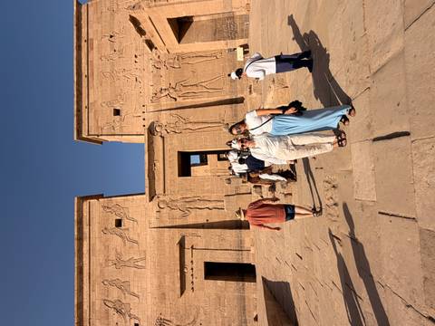       Visitors walking across the stone courtyard of an ancient Egyptian temple with detailed reliefs
  