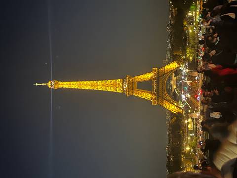      Nighttime Eiffel Tower illuminated in gold above a bustling plaza
  