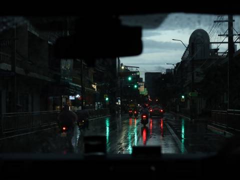       A rain-soaked city street at night, seen through a car’s wet windshield with reflections on the pavement.
  