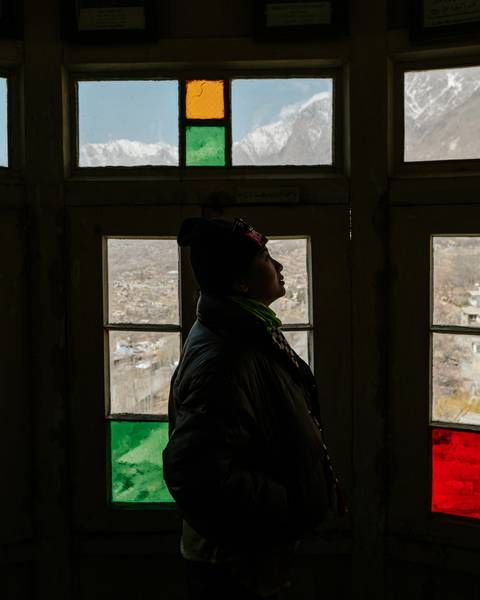       A back-lit traveller in winter clothing gazes out of old wooden window frames over a remote valley.
  