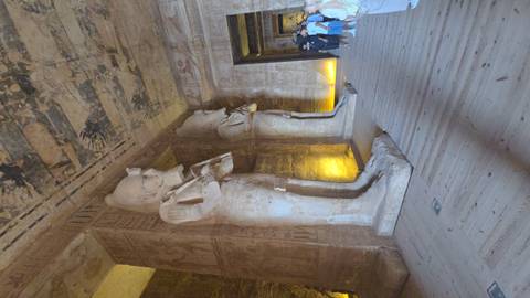       Colossal statues line the sandstone interior hall of Abu Simbel temple illuminated by warm lighting.
  
