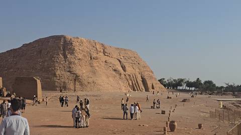       Visitors walk across the sandy forecourt of Abu Simbel’s rock-cut façade under a cloudless sky.
  