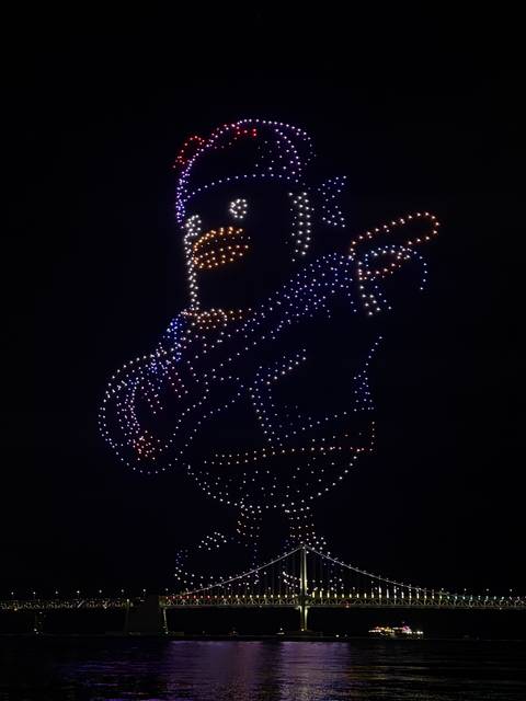       Night drone light show forming an animated bear playing guitar with bright dots.
  