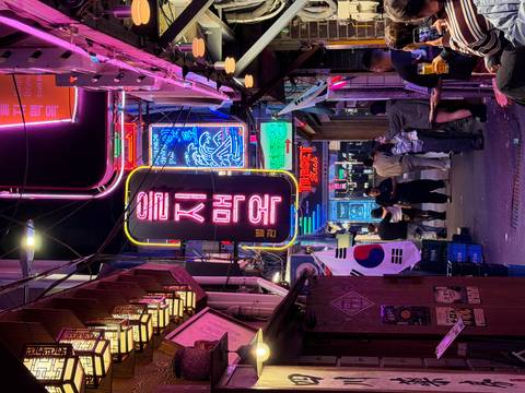       Vibrant neon alley in a Korean nightlife district with people socialising beneath the lights.
  