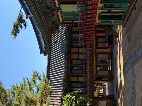       Quiet temple courtyard with colourful wooden balconies and tiled roofs in soft light.
  