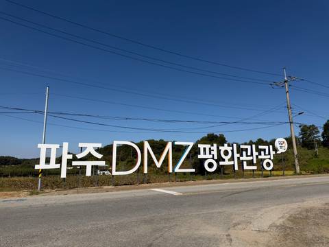       Large roadside sign for the Paju DMZ Peace Tourism area against a clear blue sky.
  