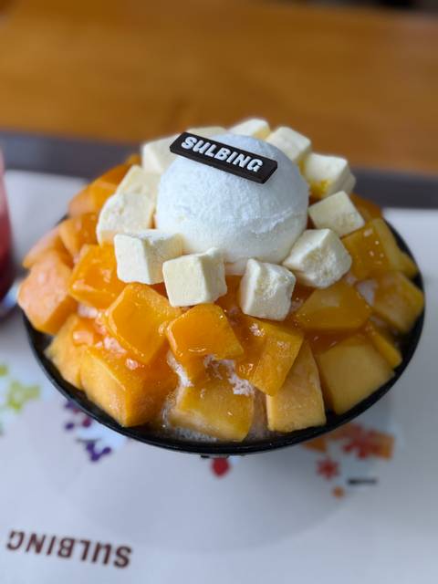       Close-up of mango bingsu dessert topped with vanilla ice cream and chewy cubes.
  