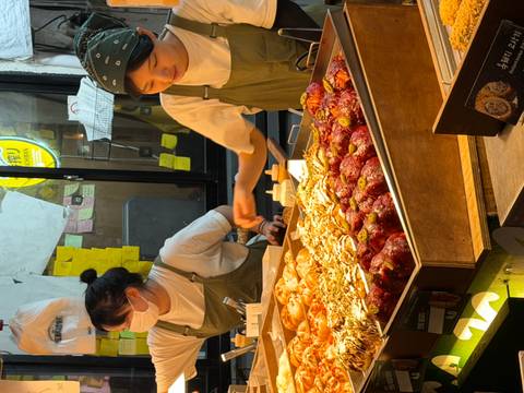       Night market food stall with two vendor women serving trays of colorful street food.
  