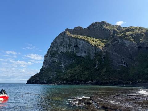       Imposing volcanic cliff rises above clear turquoise sea on Jeju Island.
  