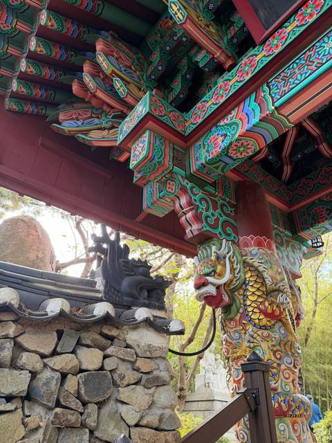       Vibrantly painted wooden eaves and guardian dragon sculpture of a Korean temple gate.
  