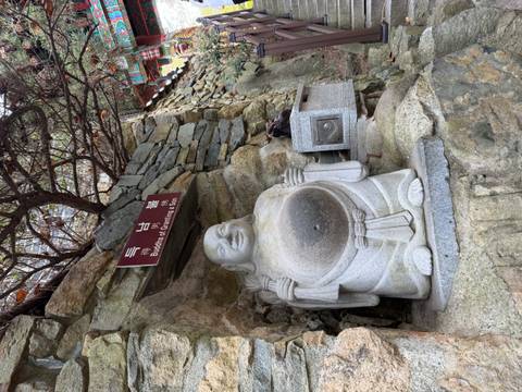       Stone Buddha of Granting a Son statue set into a rocky wall beside a sign.
  