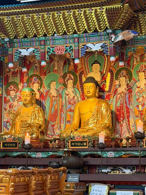       Ornate golden Buddha statues sit before a richly decorated temple backdrop.
  