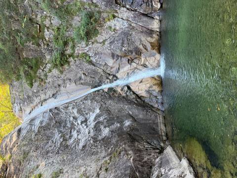       Narrow waterfall cascades into an emerald forest pool among rocky cliffs.
  
