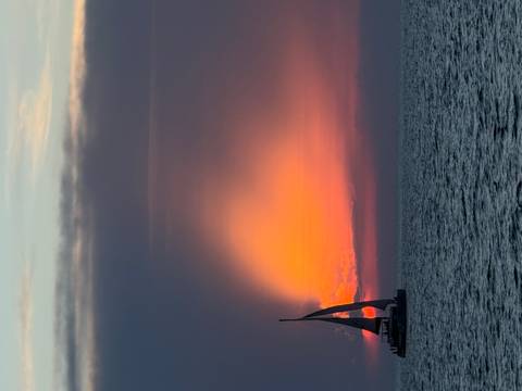       A lone sailboat passes before a dramatic orange sunset glow over the open sea.
  