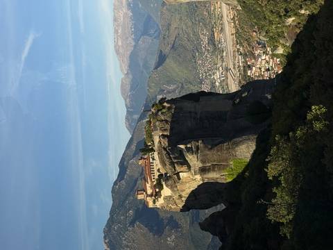       Monastery perched atop a massive rock pillar in the Meteora region with mountains in the background.
  