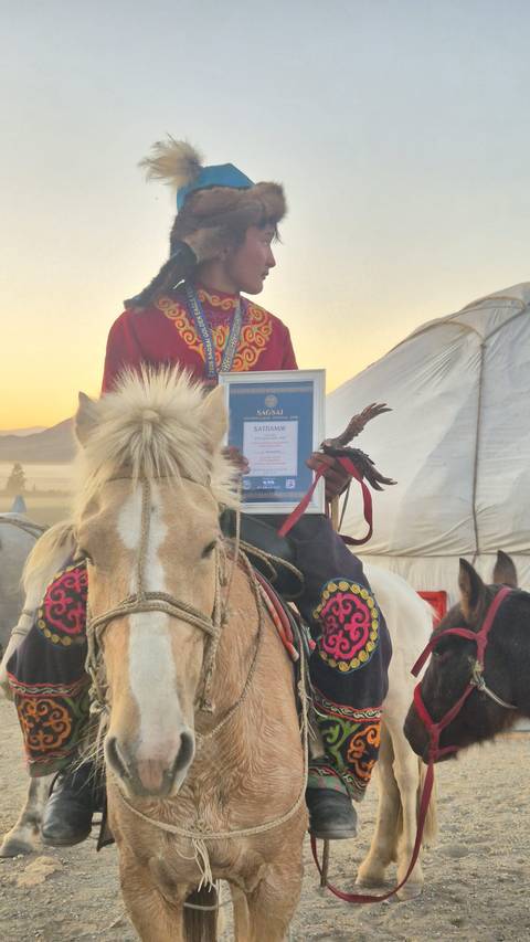       Mounted participant proudly displays a framed certificate and eagle trophy beside a traditional ger.
  