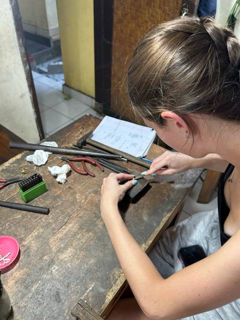       Participant crafting jewelry with hand tools on a wooden workbench during a silversmith workshop.
  