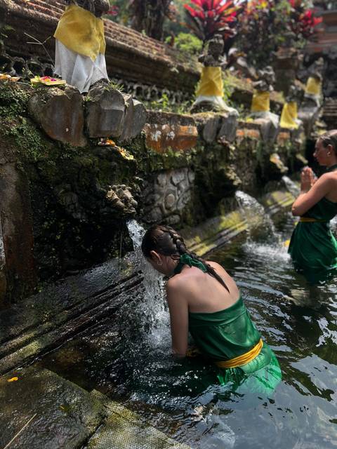       Women dressed in green sarongs take part in a purification ritual under stone spouts at a Balinese water temple.
  