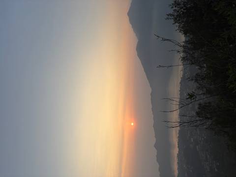       Serene sunrise over a misty lake and volcanic mountain ridge, viewed from a hillside.
  