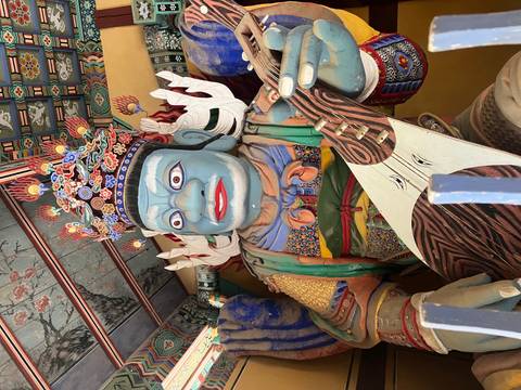       Colorful guardian deity statue inside an ornate Korean temple with intricate ceiling patterns.
  