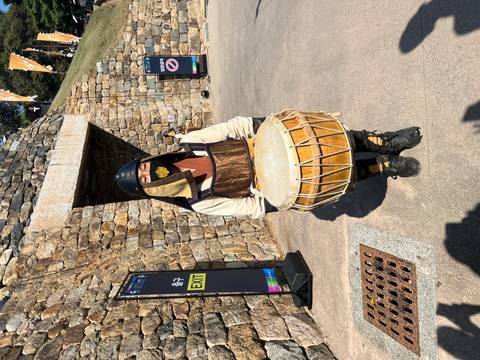       Costumed performer in traditional armor holds a drum outside fortress walls at a heritage event.
  
