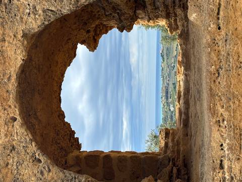       Rocky arch frames a sweeping view of rolling countryside and distant coastline under a moody sky.
  