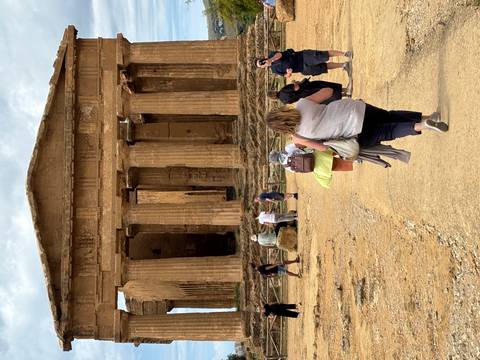       Visitors stroll a sandy path toward massive Doric columns of an ancient Greek temple ruin.
  