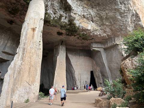       Visitors gather beneath towering limestone walls at the dramatic entrance of a cavernous quarry.
  