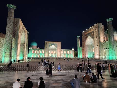       Illuminated Registan Square with its magnificent madrasas glowing green against the night sky.
  