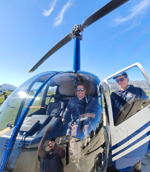       Traveller seated in a helicopter cockpit prepares for scenic flight with pilot beside.
  