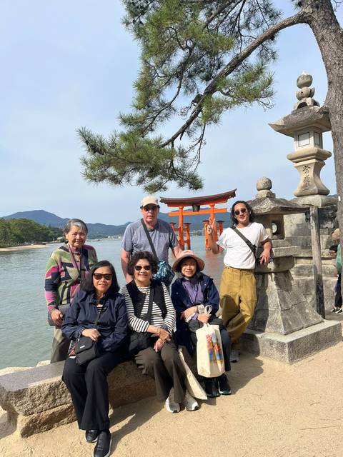       Group poses by Miyajima’s famous floating torii gate beside a stone lantern.
  