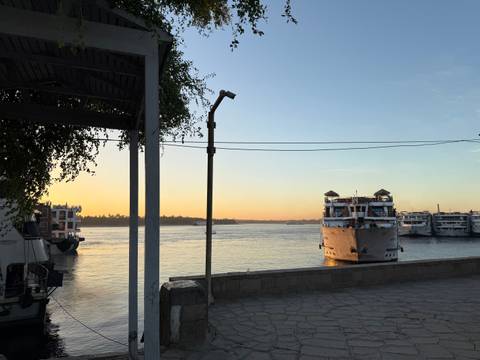       Cruise boats moored on a calm river as the sky glows orange at sunset, framed by a pier and lamppost
  