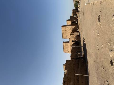       Wide view of an ancient desert temple complex with carved reliefs and sandy foreground under a clear sky
  