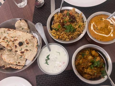       Spread of Indian dishes including naan, biryani, curry and raita on a wooden table
  