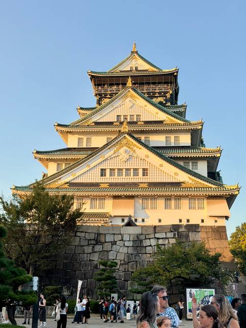       Close-up of ornate white-and-green Osaka Castle glowing in warm evening light.
  