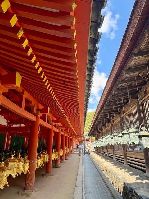       Vivid vermilion temple corridor with hanging bronze lanterns under blue sky.
  