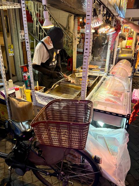       Street-food vendor grills skewers at a bustling night market stall.
  