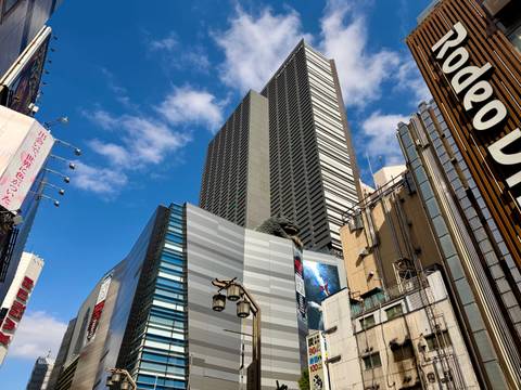       Modern skyscraper district in Tokyo with Godzilla head peering from rooftop.
  