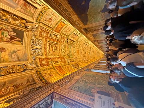       Crowds walk beneath the ornately frescoed golden ceiling of the Vatican’s Gallery of Maps.
  