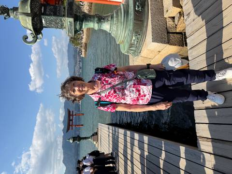       Visitor posing on a pier with the iconic floating torii gate of Itsukushima Shrine across the bay.
  