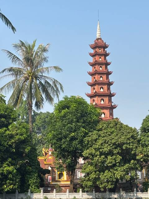       Brick pagoda tower rising above tropical trees with clear blue sky
  