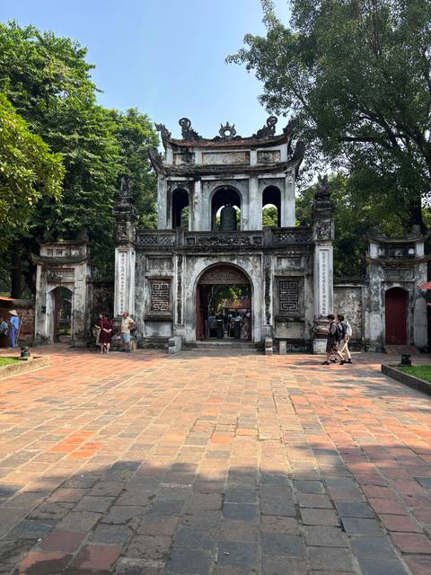       Stone gateway of the Temple of Literature with tourists walking through the courtyard
  