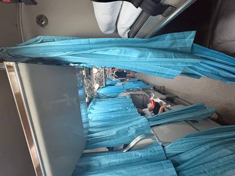       Narrow aisle of an overnight train with blue privacy curtains and passengers settling into bunk beds.
  
