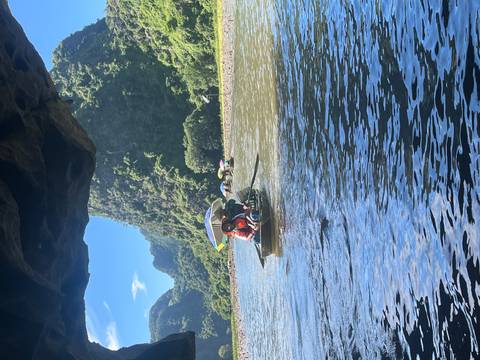       Small rowboats emerging from a cave onto a sunlit river flanked by dramatic karst peaks.
  