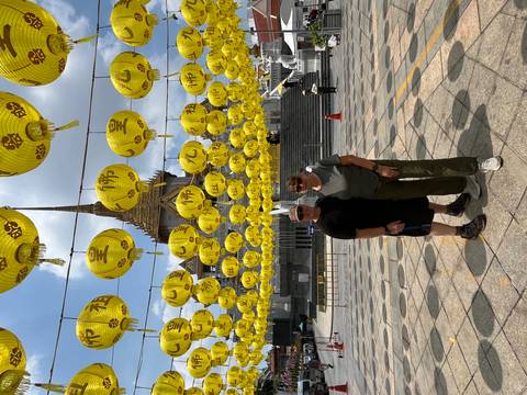       Travellers standing beneath rows of bright yellow lanterns in front of an ornate Thai temple.
  