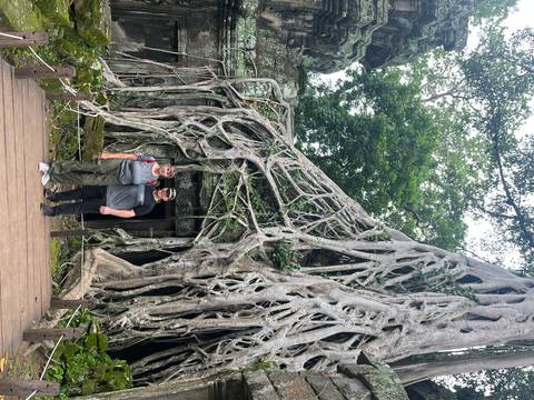       Couple standing beneath massive strangler-fig roots enveloping an ancient temple doorway.
  