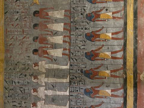      Colorful wall paintings of ancient Egyptian figures and hieroglyphs preserved inside a tomb.
  