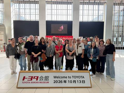       Large tour group posing inside Toyota museum lobby with bilingual welcome sign.
  